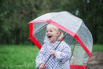 Photo 1: a child standing outdoors in rainy weather under a transparent umbrella