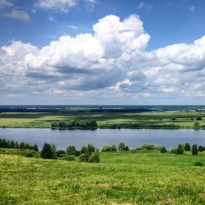 Пейзаж с рекой, зелёными полями, лугом и облачным небом